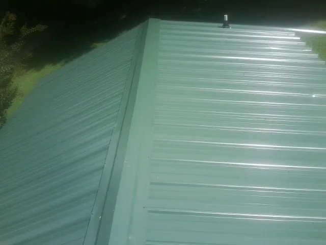 New green metal panels meeting at the ridge of a roof — Flat Roof Repair work by our crew in Ogunquit