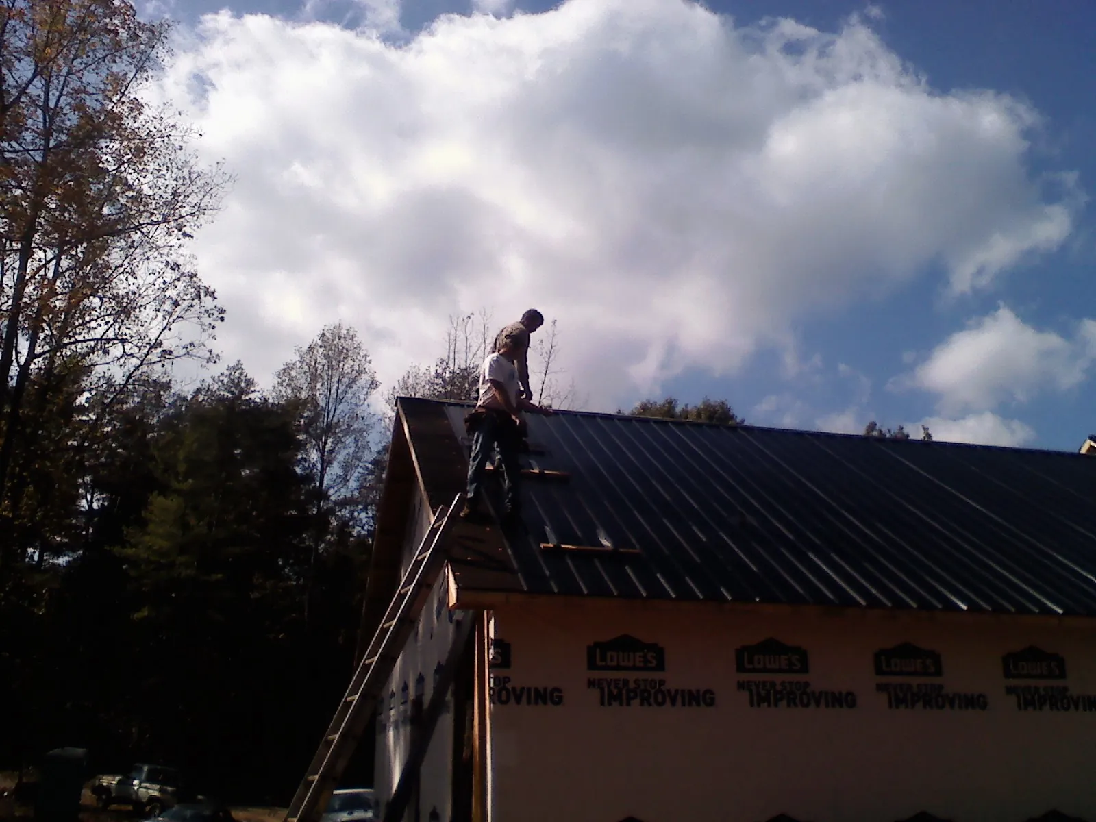 Roofer fastening dark metal panels high against a cloudy sky, from a Roof Inspection job in Ogunquit